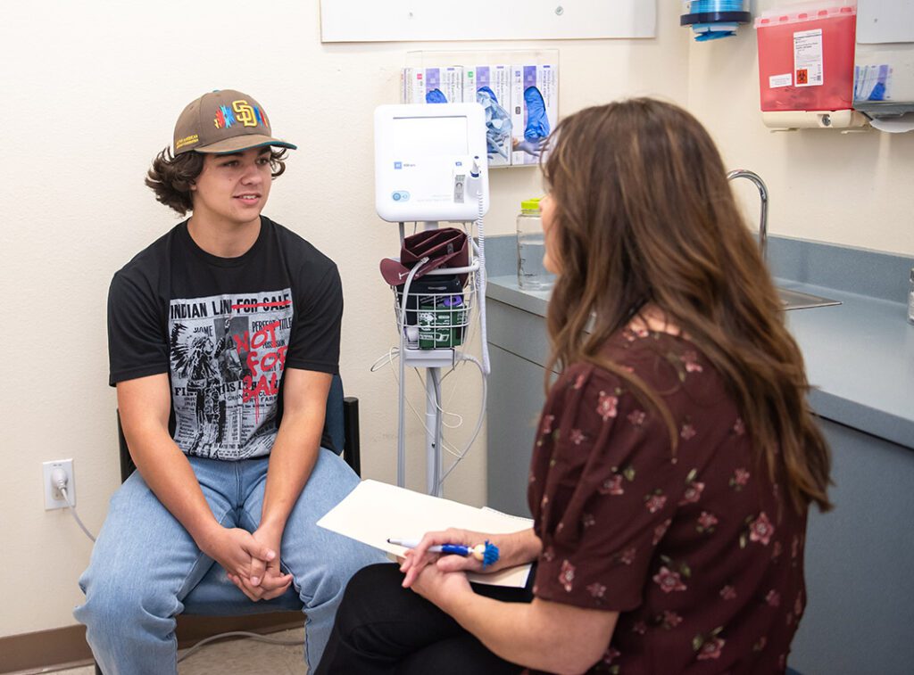 A teenager talking to a counselor inside a clinic room.